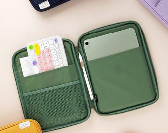 May include: An open green zippered case with a mesh pocket, a white keyboard with colorful keys, and a white stylus in the other pocket. The case is lined with a green fabric and has a zipper closure. The case is open and the keyboard is visible. The case is sitting on a light pink surface.