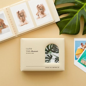 May include: A cream-coloured photo album with the text "I LOVE THIS Moment." and a decorative leaf cutout. The album is open, displaying several photos of dogs. Two additional photos of dogs are on the right.