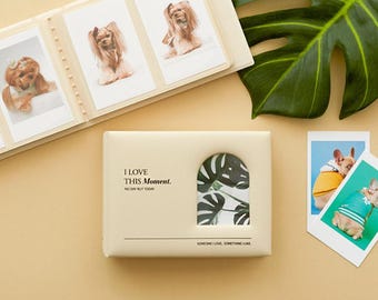 May include: A cream-colored photo album with the text "I LOVE THIS Moment." and a decorative leaf cutout. The album is open, displaying several photos of dogs. Two additional photos of dogs are on the right.
