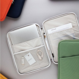 May include: A set of six laptop sleeves in various colors, including orange, navy blue, lavender, green, and yellow. The sleeves are made of a soft, durable fabric and feature a zipper closure. The interior of one sleeve is shown, revealing a mesh pocket and a zippered pocket. The text "Study Guide" is visible on a document inside the sleeve.