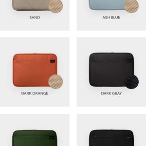 May include: Six laptop sleeves in a variety of colours: sand, ash blue, dark orange, dark grey, khaki, and black. Each sleeve features a zipper closure and a small pocket on the front. The sleeves are lined with a soft, padded material to protect your laptop.