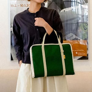 May include: A green canvas tote bag with white trim and straps. The bag has a zipper closure and a small pocket on the front.
