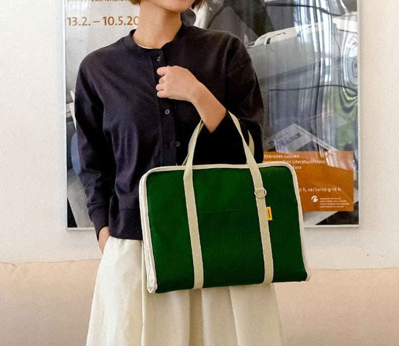 May include: A green canvas tote bag with white trim and straps. The bag has a zipper closure and a small pocket on the front.
