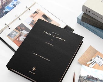 May include: Black photo album with the title "Pieces of Moment for My Memories" and the text "Life is made of small moments like this". The album is closed and has a gold leaf design on the front cover.