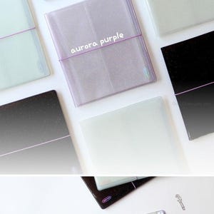 Może przedstawiać: Zestaw sześciu przezroczystych album&oacute;w fotograficznych z plastiku z r&oacute;żnymi błyszczącymi tłami. Albumy są oznaczone jako "dark galaxy", "milky way", "aurora purple" i trzy inne kolory. Albumy są otwarte, aby pokazać przezroczyste plastikowe strony wewnątrz.
