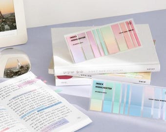 May include: Two packs of pastel colored index highlighter sticky notes. Each pack contains 20 sheets of sticky notes. The top pack has a spring theme and the bottom pack has a winter theme. The sticky notes are in a clear plastic case.
