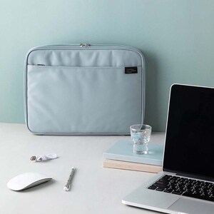May include: A light blue laptop sleeve with a zip fastening and a small pocket on the front. The sleeve is sitting on a white surface next to a laptop, a glass, and a stack of notebooks.