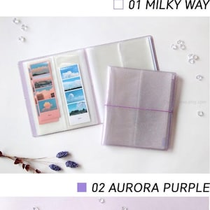 Może przedstawiać: Trzy przezroczyste albumy fotograficzne z plastikowymi akcentami z brokatem w r&oacute;żnych kolorach. Albumy są zamknięte i pokazują okładkę. Kolory to Droga Mleczna, fioletowy aurora i ciemna galaktyka.