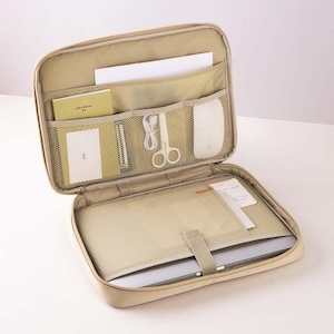 May include: Beige laptop carrying case with multiple compartments and pockets. The case is open and a laptop, mouse, scissors, and other items are visible inside.