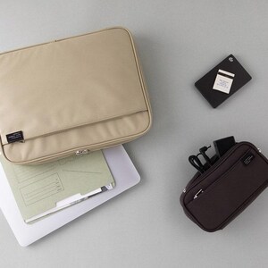 May include: Two zippered pouches in beige and brown. The larger pouch is open and contains a white folder. The smaller pouch has a zippered pocket and is filled with cords and a black phone charger.