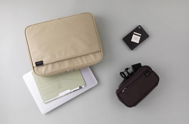May include: Two zippered pouches in beige and brown. The larger pouch is open and contains a white folder. The smaller pouch has a zippered pocket and is filled with cords and a black phone charger.
