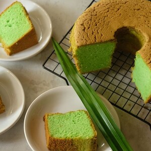 May include: A green and brown chiffon cake with a hole in the center, sliced into pieces and served on white plates. The cake is on a black wire rack with a green leaf.