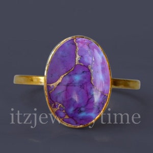 May include: A gold ring with a purple and blue oval gemstone. The gemstone has a marbled pattern with gold veins.