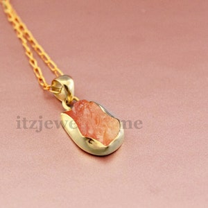 Puede incluir: Un collar de cadena de oro con un colgante que presenta una piedra preciosa de color rojo anaranjado en bruto engastada en un engaste de oro.