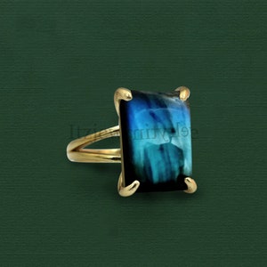May include: A gold ring featuring a square blue and black gemstone. The ring has a simple design and is set in a gold band.