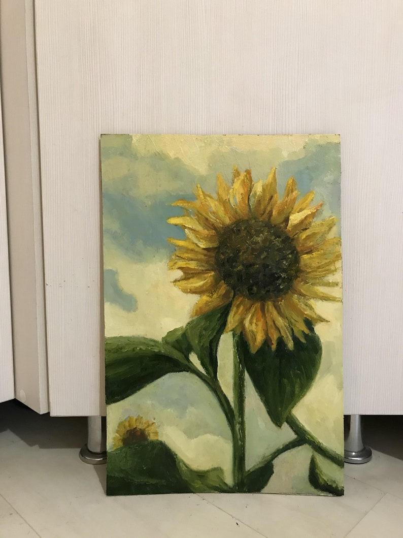 May include: A painting of a sunflower with yellow petals and a dark brown center. The sunflower is in the foreground of the painting, with a blue sky and white clouds in the background. The sunflower is painted in a realistic style, with visible brushstrokes.