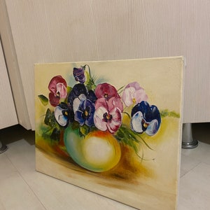 May include: A painting of a bouquet of purple, pink, and white pansies in a green vase. The pansies are arranged in a loose, natural style, and the vase is a simple, rounded shape. The background is a soft, yellow-toned canvas.