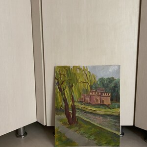 May include: A painting depicting a pink building with a moat and a weeping willow in the foreground. The building has a green roof and is surrounded by green trees. The painting is executed in a realistic style.