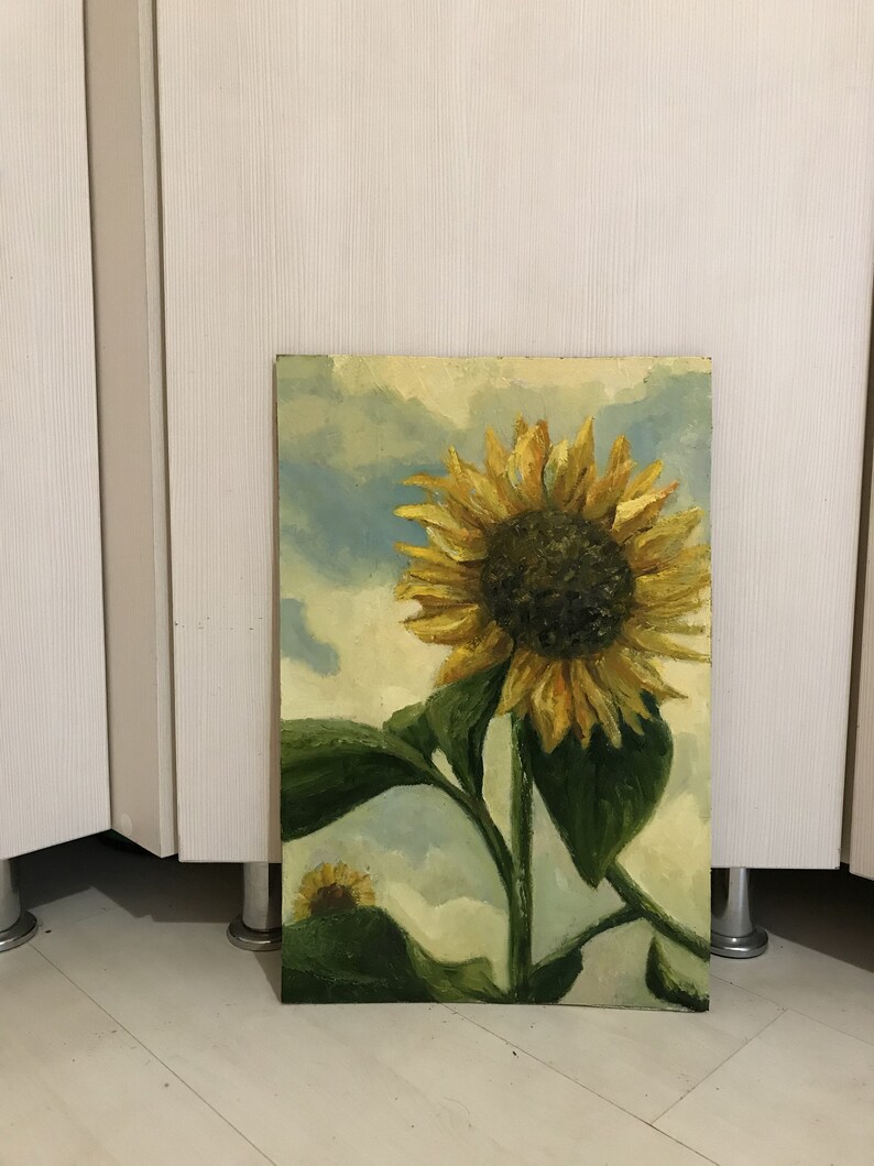 May include: A painting of a sunflower with yellow petals and a dark brown center. The sunflower is against a blue and white cloudy sky. The painting is on a canvas and has a wooden frame.