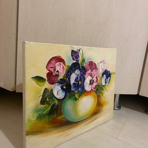May include: A painting of a bouquet of purple, pink, and white pansies in a green vase. The pansies are arranged in a loose, natural style, and the vase is a simple, rounded shape. The background is a soft yellow.