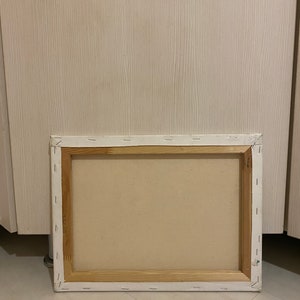 May include: The back of a stretched canvas painting with a wooden frame. The canvas is white and the frame is a light brown color.