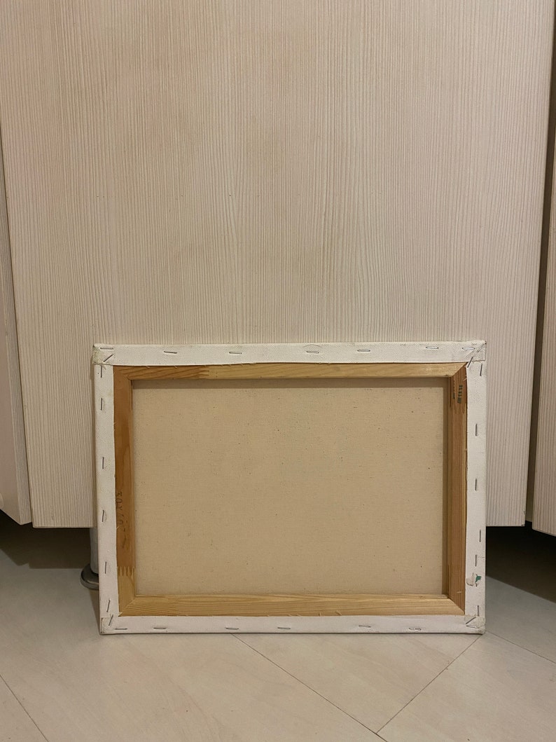 May include: The back of a stretched canvas painting with a wooden frame. The canvas is white and the frame is a light brown color.