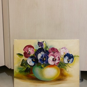 May include: A painting of a bouquet of purple, pink, and white pansies in a green vase. The pansies are arranged in a loose, natural style, and the vase is simple and elegant. The background is a soft, cream color.