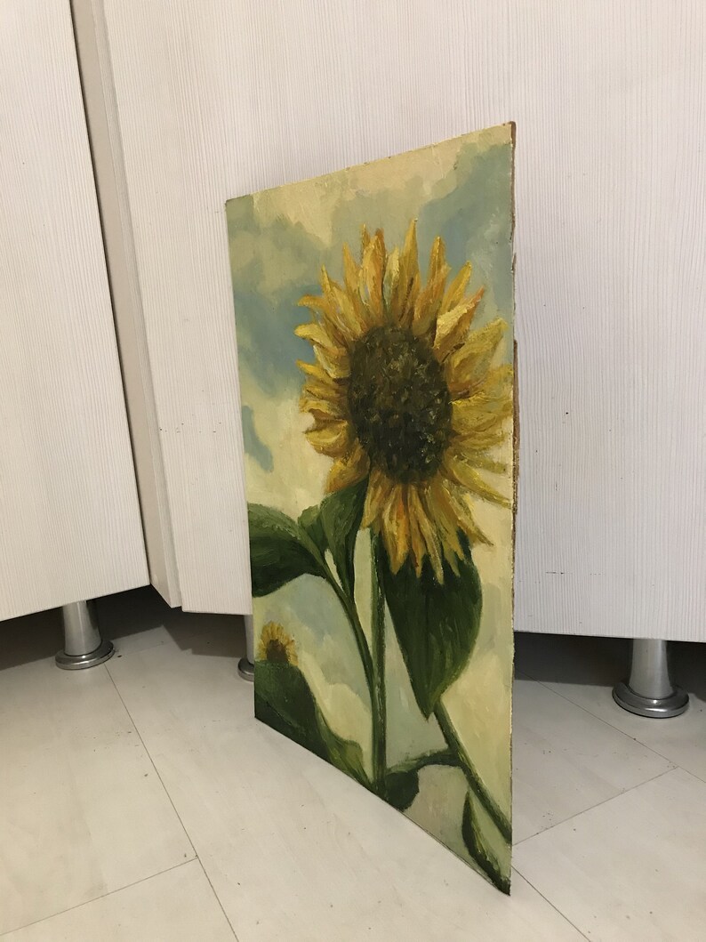 May include: A painting of a sunflower with yellow petals and a dark brown center. The sunflower is against a background of blue and white clouds.