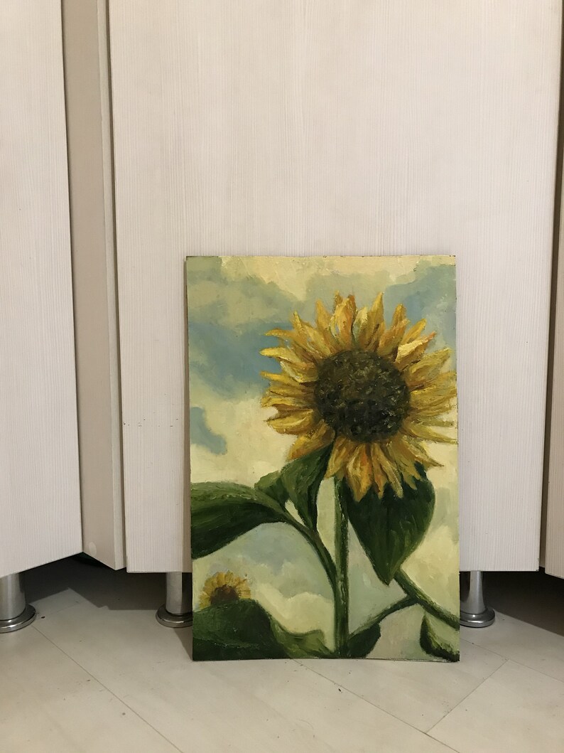 May include: A painting of a sunflower with a yellow center and yellow petals. The sunflower is against a blue and white cloudy sky. The sunflower is in a field of green leaves.