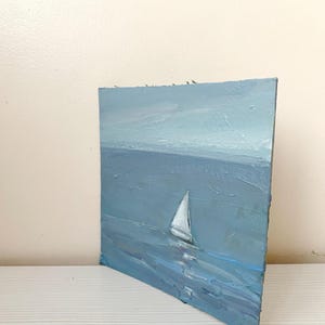 May include: A painting of a sailboat on a blue ocean with a light blue sky in the background.