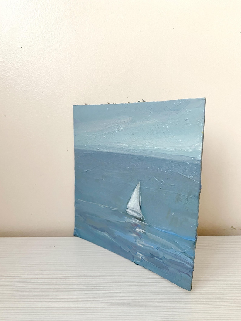 May include: A painting of a sailboat on a blue ocean with a light blue sky in the background.