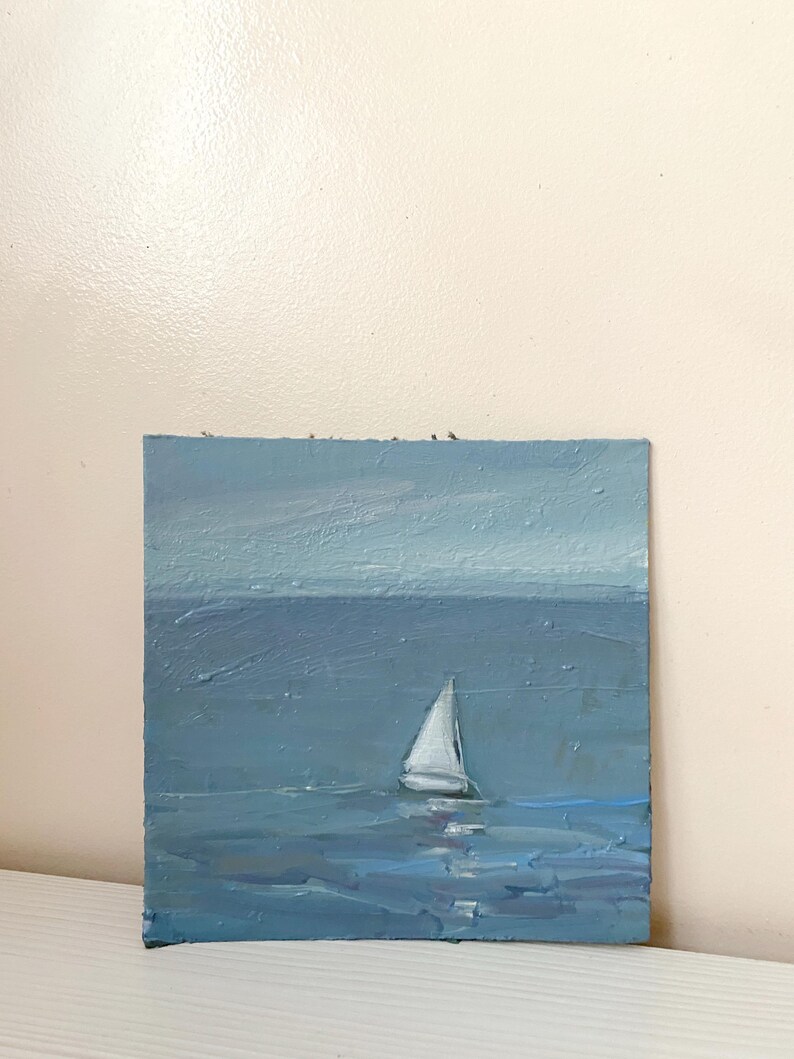May include: A small oil painting of a sailboat on a blue sea with a light blue sky in the background.
