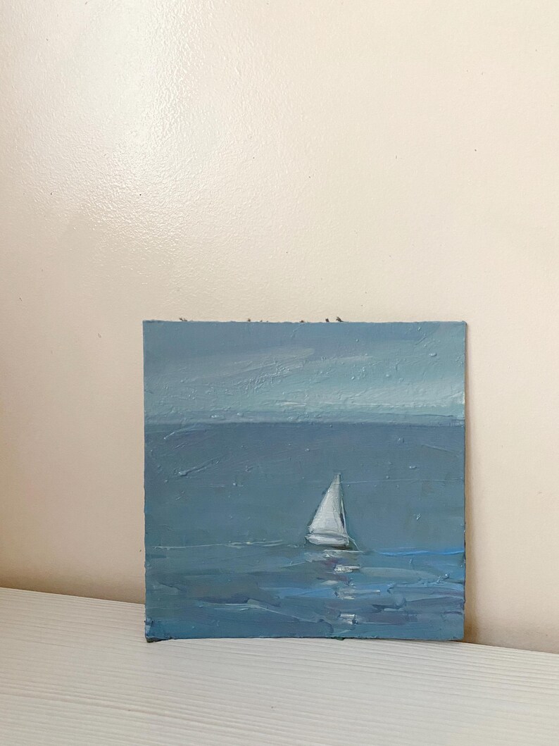 May include: A small oil painting of a sailboat on a blue sea with a light blue sky in the background.