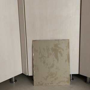 May include: A close-up of a light brown cardboard sheet with water stains. The sheet is lying on a light brown wooden floor.