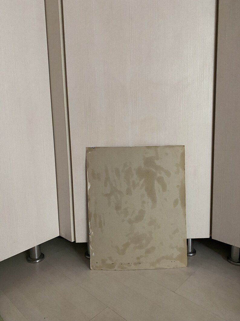 May include: A close-up of a light brown cardboard sheet with water stains. The sheet is lying on a light brown wooden floor.
