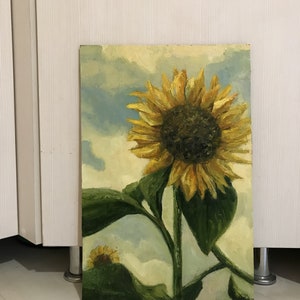 May include: A painting of a sunflower with yellow petals and a dark brown center. The sunflower is against a blue and white cloudy sky. The painting is on a canvas.