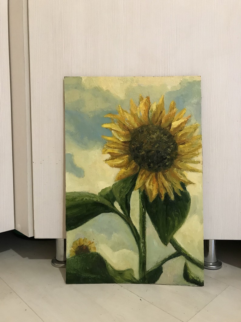 May include: A painting of a sunflower with yellow petals and a dark brown center. The sunflower is against a blue and white cloudy sky. The painting is on a canvas.