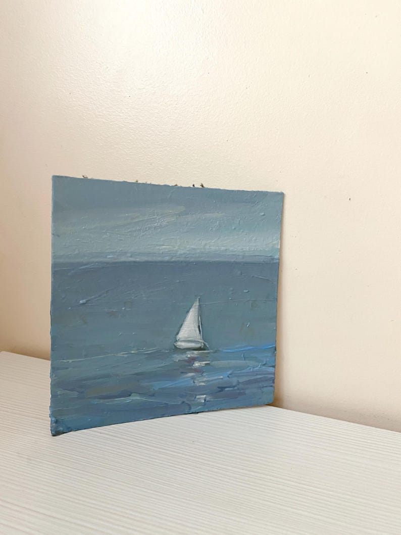 May include: A small painting of a sailboat on a blue sea with a light blue sky. The sailboat is white and has a single sail.