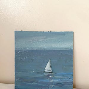 May include: A painting of a sailboat on a blue ocean with a light blue sky in the background.