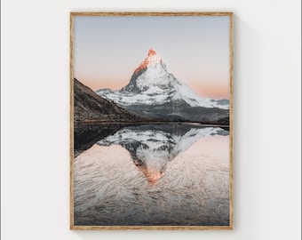 May include: A snowy mountain peak reflected in a still lake. The mountain is a vibrant orange at the summit, with a soft pink sky in the background.