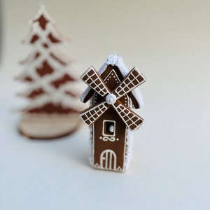 May include: A gingerbread windmill with white icing and a brown roof. The windmill has a white door and a window. The windmill is decorated with white dots.