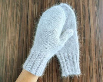 Può includere: Un paio di guanti di lana grigi con una texture soffice. I guanti sono piegati insieme e si trovano su una superficie di legno.