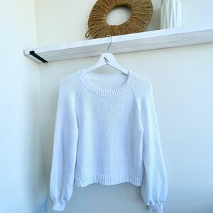 K&ouml;nnte beinhalten: Ein einfarbiger wei&szlig;er Langarmpullover mit Rundhalsausschnitt, gerippten B&uuml;ndchen und einem gerippten Saum. Das Kleidungsst&uuml;ck ist in Strickoptik gefertigt und wird auf einem wei&szlig;en Kleiderb&uuml;gel pr&auml;sentiert, was ein schlichtes Design mit &Auml;rmeln zeigt.