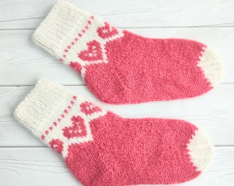 May include: A pair of pink and white knitted socks with a heart pattern. The socks are made of soft yarn and have a comfortable fit.