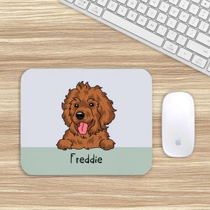 May include: A rectangular mouse mat with a cartoon illustration of a brown dog with its tongue out. The dog's name, "Freddie," is printed in black at the bottom. A white mouse and keyboard are also visible.