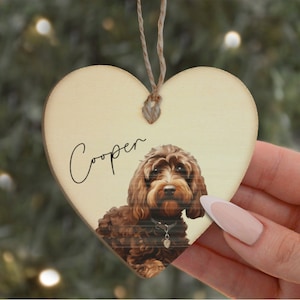 May include: A wooden heart-shaped ornament featuring a brown dog. The dog's name, "Cooper", is written in cursive on the ornament.