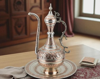 May include: An ornate copper and silver pitcher with a long spout and decorative handle. The pitcher sits on a matching plate with a floral design. The piece is likely used for serving beverages and is a decorative item.