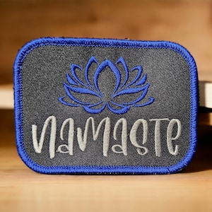 May include: A black embroidered patch with a blue lotus flower and the word "namaste" in silver thread.