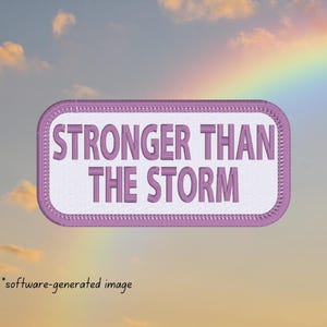 May include: A pink and white embroidered patch with the text "Stronger Than The Storm".