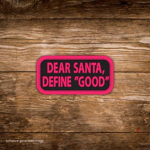 May include: A rectangular patch with the text "DEAR SANTA, DEFINE "GOOD"" in bright pink letters on a black background. The patch has a pink border and is set against a wooden background.